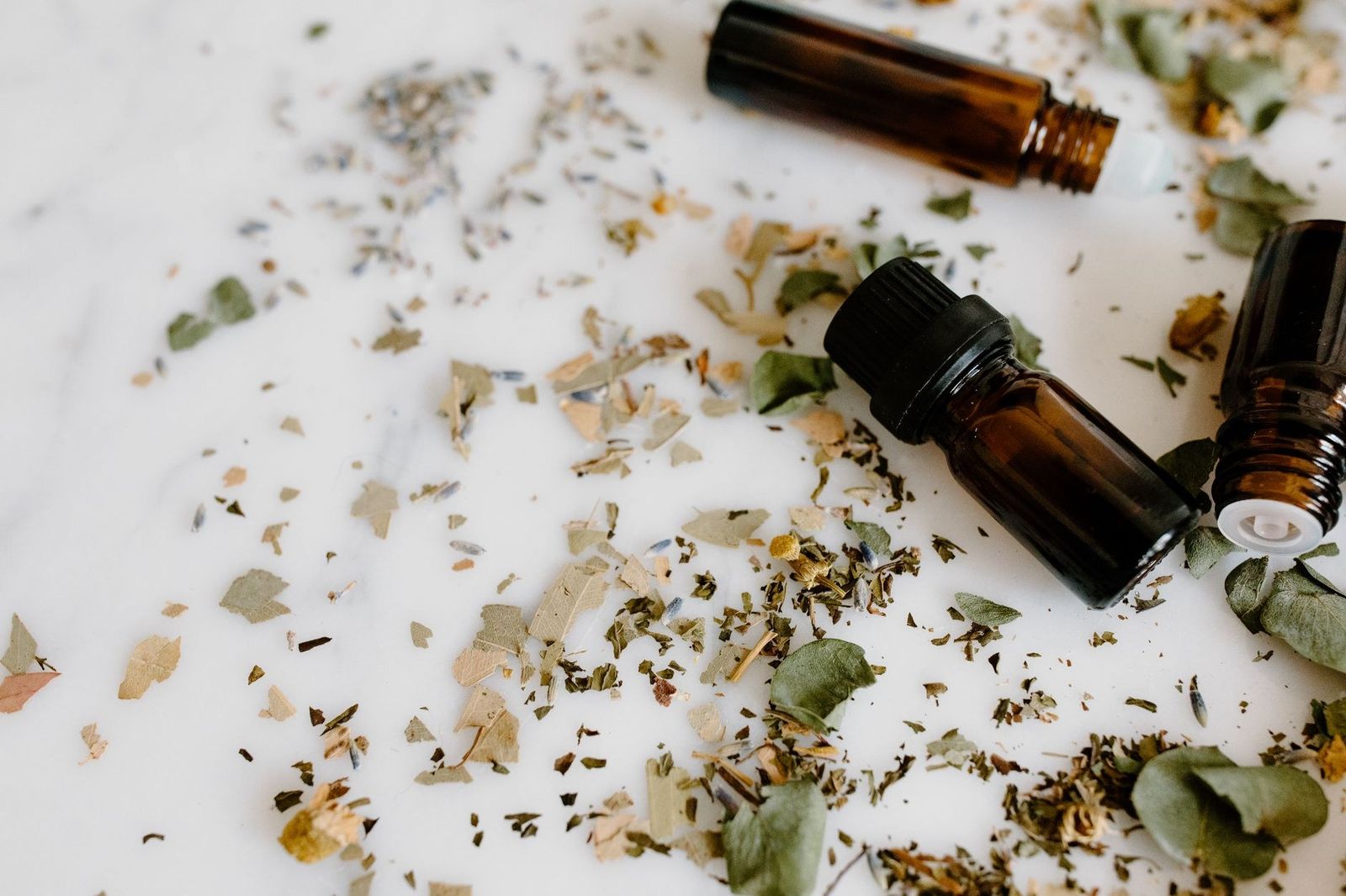 Frascos de aceites esenciales con hierbas secas sobre una superficie blanca