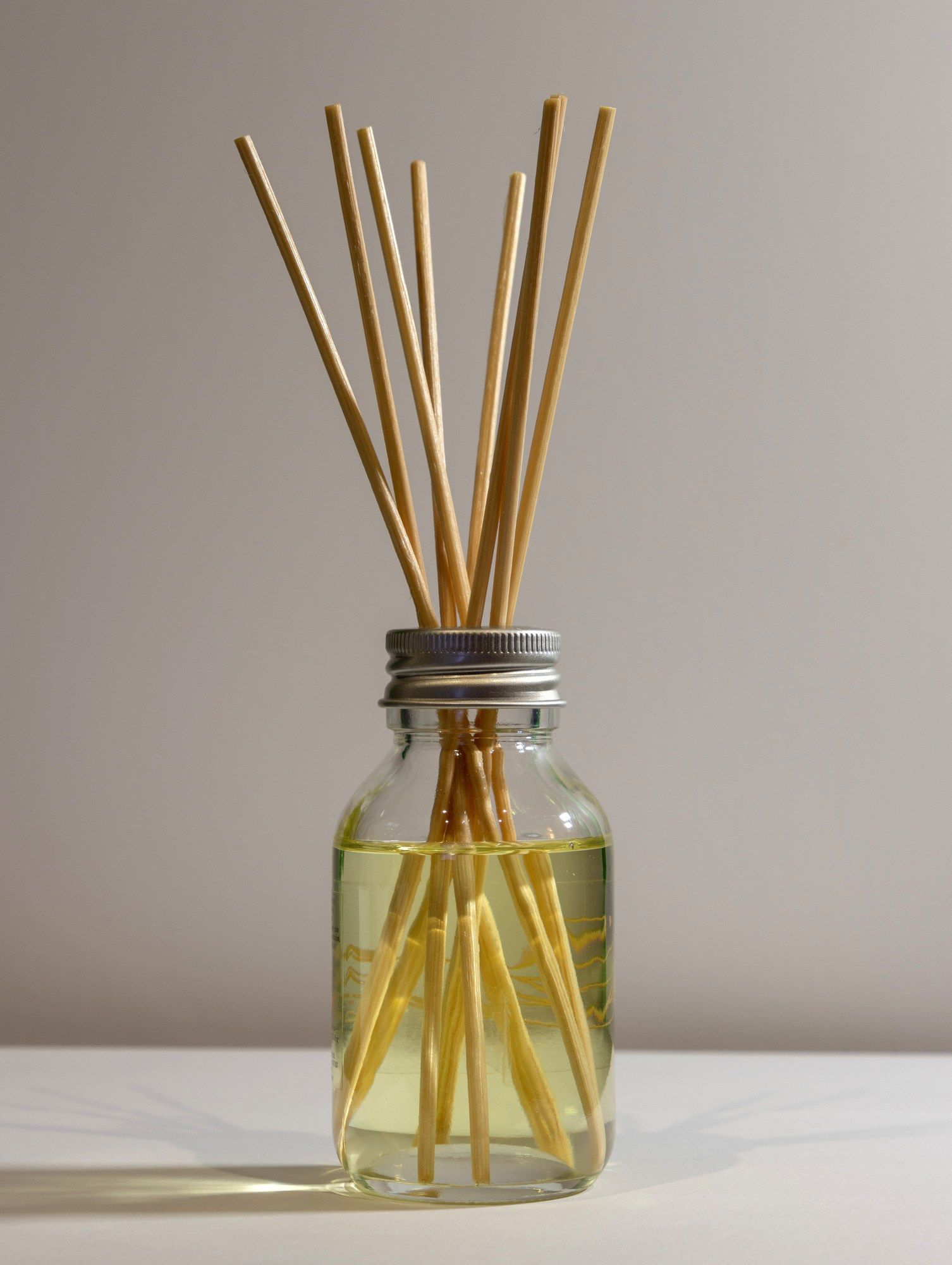 Difusor de varillas minimalista en frasco de vidrio con líquido aromático sobre fondo gris