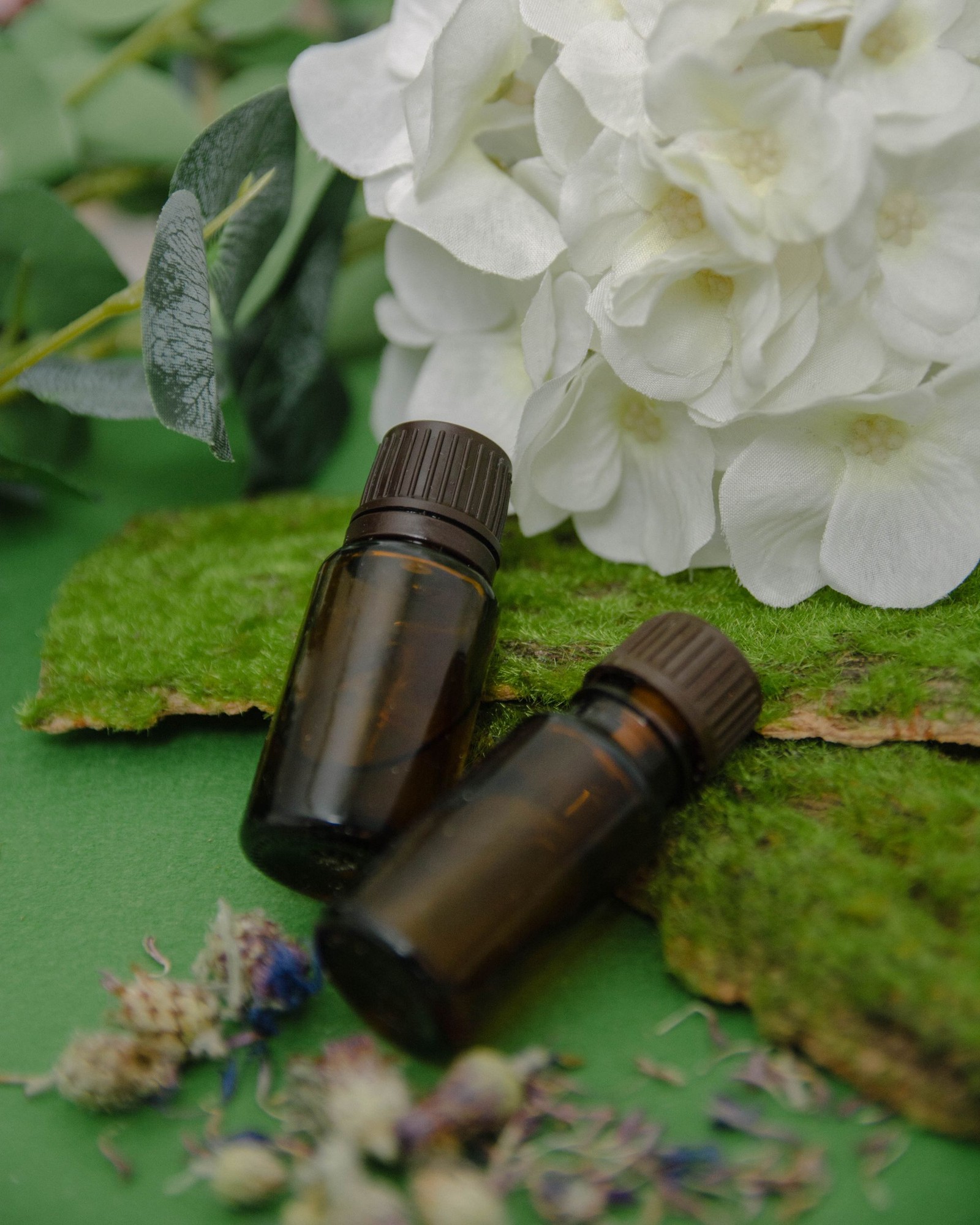 Frascos de aceite esencial apoyados sobre musgo con flores blancas