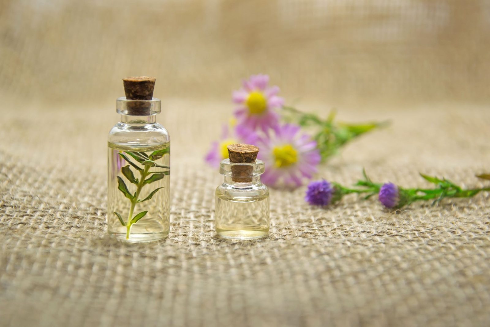 Frascos de aceites esenciales y flores frescas sobre una tela de arpillera